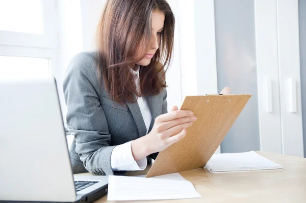 Beautiful business woman looking at papers she holding in her arms while wo — Stock Photo, Image