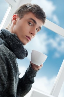 kahve içme ve kamera, parlak gökyüzü ve bulutlar dışında bakarak genç bir adam portresi