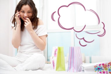 Portrait of young beautiful awake woman with gifts on bed at bedroom. Talking with her boyfriend by mobile phone. Cloud balloon overhead clipart