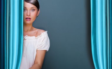 Closeup of young, pretty woman standing near curtain and holding it clipart