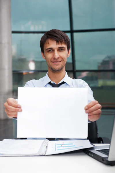 Aantrekkelijke man in het bedrijfsleven pak met leeg teken zit op zijn kantoor en lacht om camera — Stockfoto