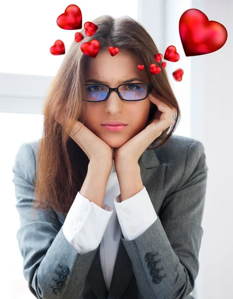Portrait of a bored serious businesswoman working at her desk with paperwork and dreaming about love. Hearts are floating around her head — Stock Photo, Image