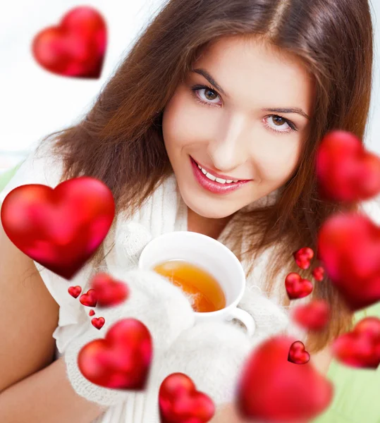 Day dreaming - Caucasian American female relaxed at home, having a cup of tea. Wearing wool scarf and gloves. Beautiful red hearts floating on foreground — Stock Photo, Image
