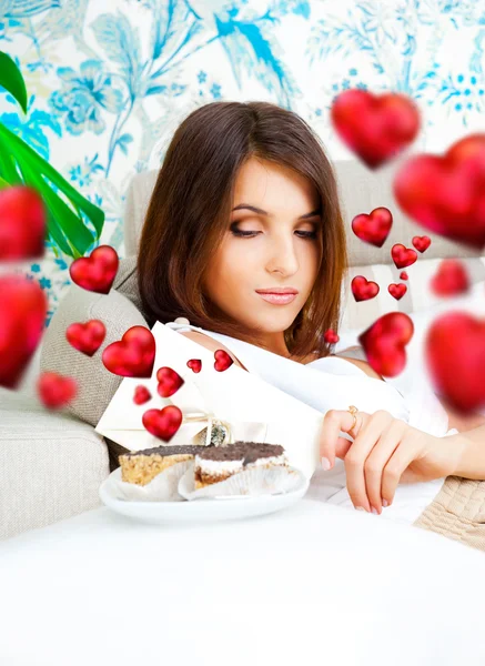 Porträt einer jungen hübschen Frau, die am Valentinstag leckere Kuchen isst und um sie herum grafische Herzen fliegen — Stockfoto