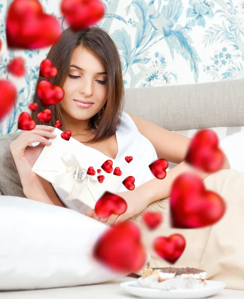 Cute young woman holds a valentine and reading it. Beautiful heart symbols flying around her. She is in love with her couple — Stock Photo, Image