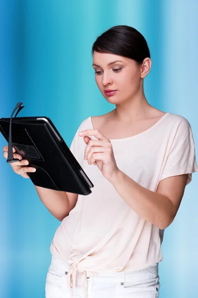 Retrato de jovem mulher bonita segurando tablet computador e óculos sorrindo de pé contra fundo digital azul — Fotografia de Stock