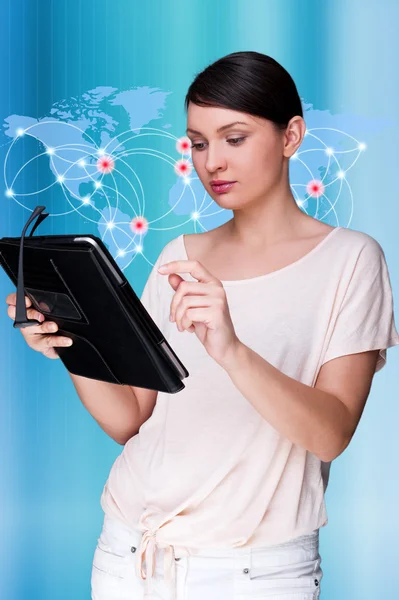 大きな世界地図の前に立っている若い女性の肖像画と彼女のタブレットコンピュータを見て。青いデジタル背景を背景に — ストック写真