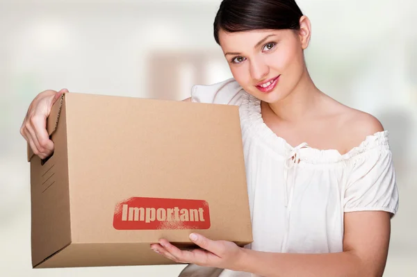 Une femme tenant une boîte à l'intérieur d'un immeuble de bureaux ou d'une maison. Panneau de paquet sur la boîte — Photo
