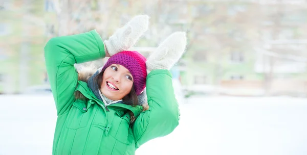 Όμορφη κοπέλα φορώντας χειμώνα ρούχα και να παίζουν σε εξωτερικούς χώρους. κρατά τα χέρια κοντά το κεφάλι της και δείχνει το αστείο κουνέλι — Φωτογραφία Αρχείου