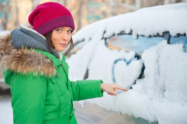 Beautiful woman in winter clothes drawing heart on car — Stock Fotó
