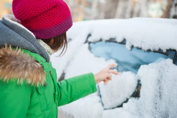 Schöne Frau in Winterkleidung zeichnet Herz auf Auto — Stockfoto