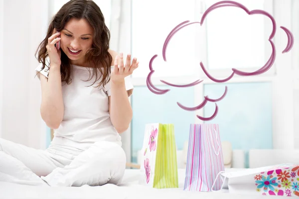 Portrait of young beautiful awake woman with gifts on bed at bedroom. Talking with her boyfriend by mobile phone. Cloud balloon overhead — Stock Photo, Image
