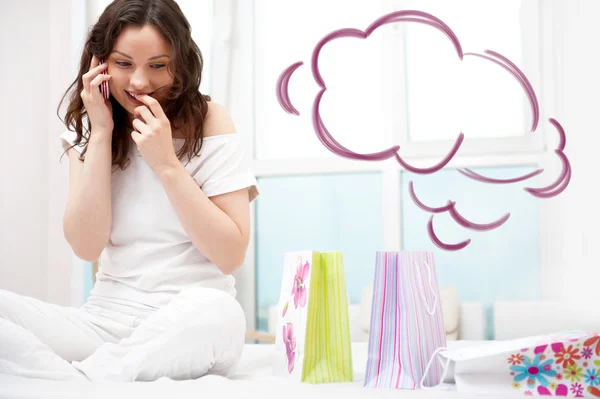 Portrait of young beautiful awake woman with gifts on bed at bedroom. Talking with her boyfriend by mobile phone. Cloud balloon overhead — Stock Photo, Image