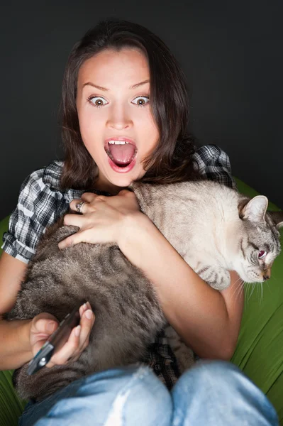 Young funny woman sitting in her beanbag and embracing her cat while watching tv. She is very scared while watching horror film in dark room — Stock Fotó