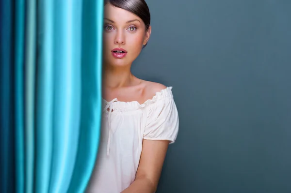 Vértes fiatal, csinos nő közelében függöny és tartása — Stock Fotó
