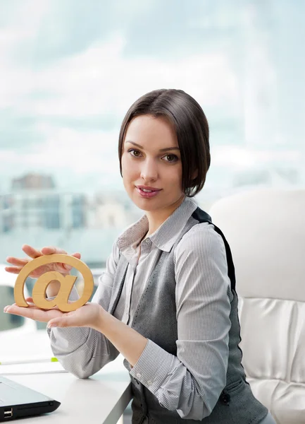 Portrait of a cheerful Business woman sitting on her desk holding an at symbol — Stock Photo, Image