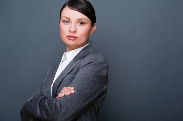 Mooie Europese jonge solide zakenvrouw die permanent met handen gevouwen tegen de grijze achtergrond — Stockfoto
