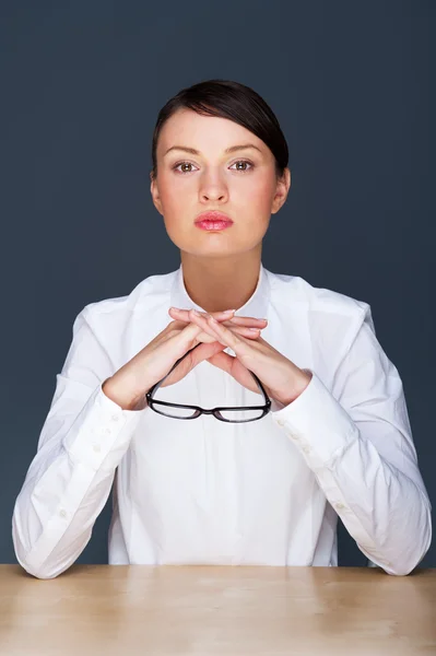 Schöne europäische junge solide Geschäftsfrau sitzt mit Brille vor grauem Hintergrund — Stockfoto