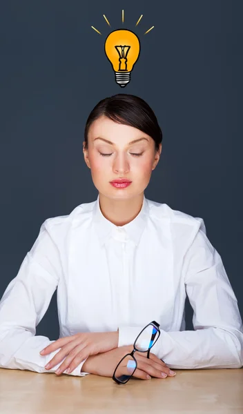 Идея женщины - мозговой штурм. Красивая деловая девушка сидит спокойно в офисе. Графическая лампа - символ новой идеи, над головой — стоковое фото