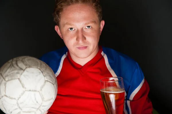 ビールとサッカー ボールを保持しているとテレビを自宅でゲームの翻訳を見て若い男スポーツウェアを着ています。 — ストック写真