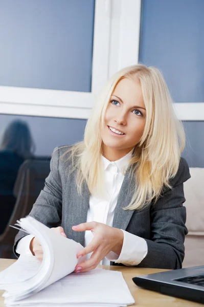 Vacker affärskvinna tittar på papper hon håller i famnen medan du arbetar med datorn på hennes kontor — Stockfoto