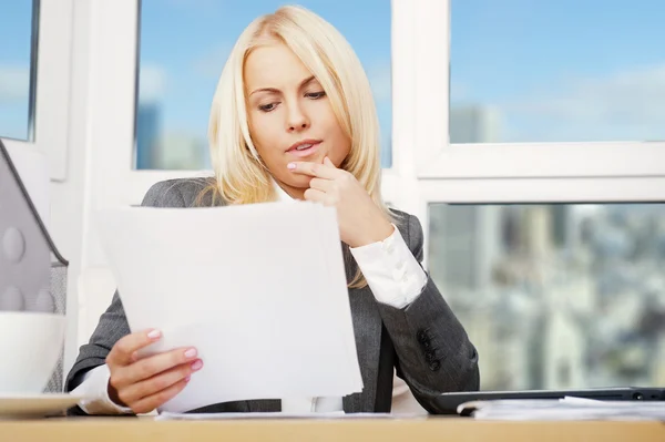 Vacker affärskvinna tittar på papper hon håller i famnen medan du arbetar med datorn på hennes kontor — Stockfoto