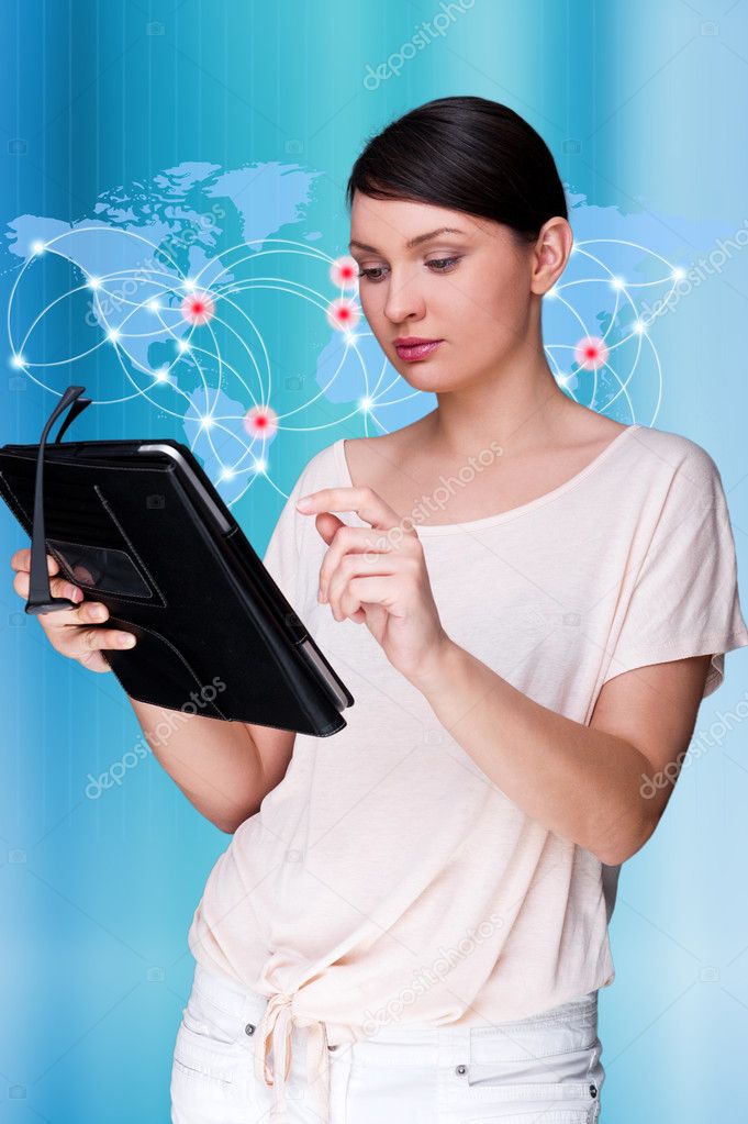 Portrait of young woman standing in front of big world map and looking at her tablet computer. Against blue digital background