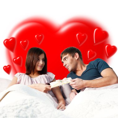 Closeup portrait of a happy young couple relaxing on the bed. Man making a gift to his girlfriend. Saint Valentine concept. Heart shape on background clipart