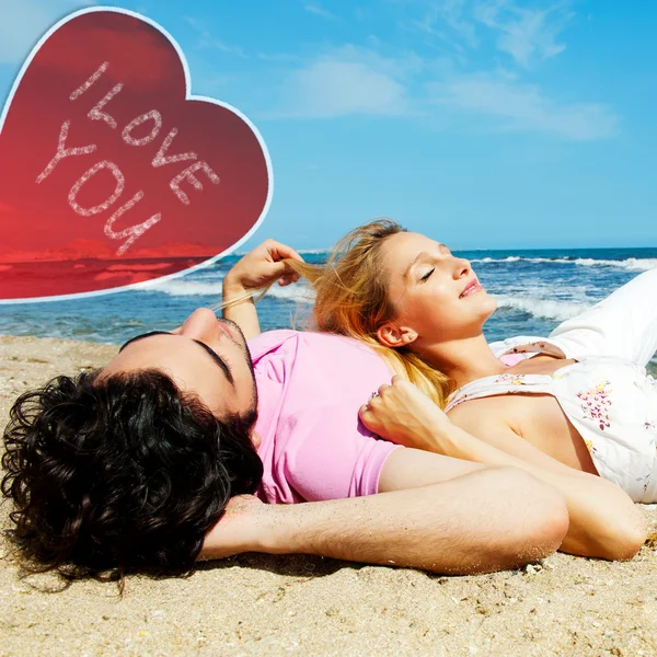 Jovem casal romântico bonito relaxante na praia no dia ensolarado. Coração e sinal eu te amo — Fotografia de Stock