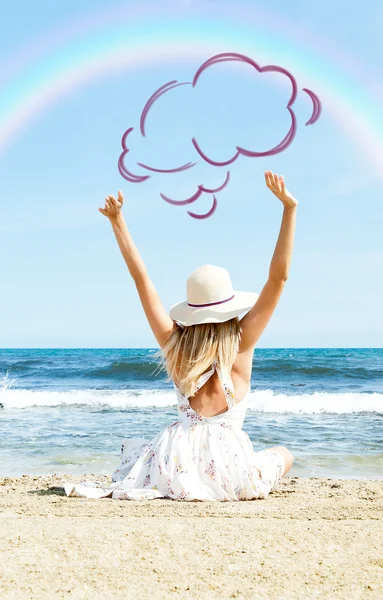 Porträt einer jungen Frau am Strand in der Nähe des Meeres, die mit erhobenen Händen in elegantem Kleid und Hut den Regenbogen betrachtet. Foto von hinten. leerer Wolkenballon über Kopf — Stockfoto