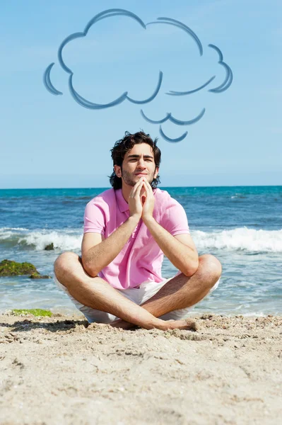 Ritratto di giovane seduto in loto posare sulla sabbia sulla spiaggia e meditare. Mare Mediterraneo sullo sfondo. Palloncino nuvoloso vuoto sopra la testa — Foto Stock