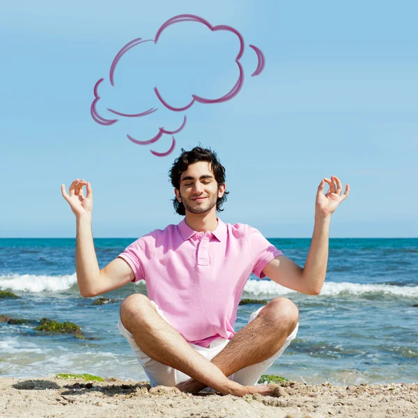 Portret van een jonge man zit in lotus pose op zand op het strand en mediteren. Middellandse Zee op de achtergrond. lege wolk ballon overhead — Stockfoto