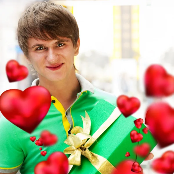 Portrait of young man inside shopping mall with gift box waiting for his girlfriend. Valentine day. Red hearts flying around — Stock Photo, Image