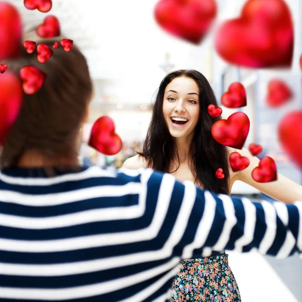 Young man meeting his girlfriend with opened arms at airport arrival hall. Red hearts around them — Stock Photo, Image