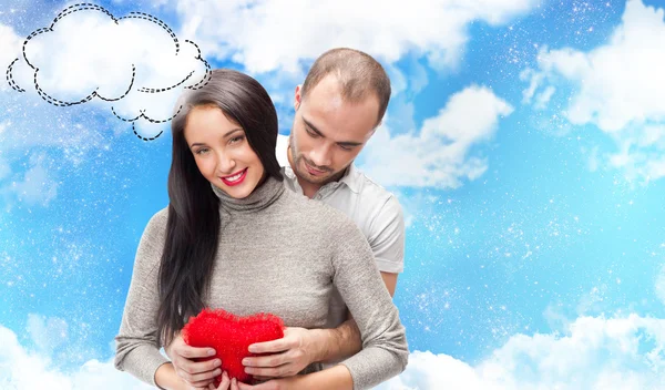 Счастливая взрослая пара с красным сердцем на романтическом фоне с небом и облаками, обнимающая и смеющаяся — стоковое фото