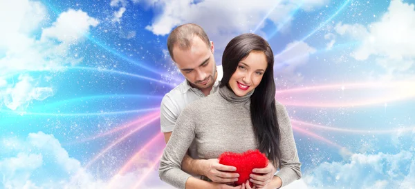 Glückliches junges erwachsenes Paar mit rotem Herz auf romantischem Hintergrund mit Himmel und Wolken, umarmt und lacht — Stockfoto