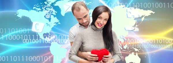 Portrait of young couple embracing and holding red heart. Standing against world map — Stock Photo, Image