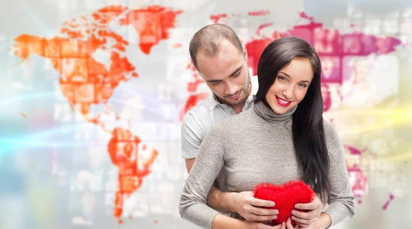 Portrait of young couple embracing and holding red heart. Standing against world map with photo of — Stock Photo, Image