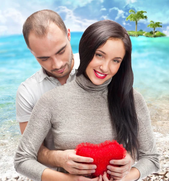 Porträt eines jungen Paares mit rotem Herz, das auf einer tropischen Insel steht und sich umarmt — Stockfoto