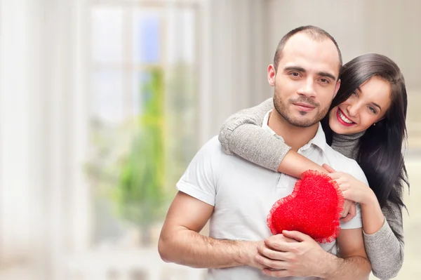 Portrét mladého páru s červeným srdcem, stojící u jejich domova a všeobjímající — Stock fotografie