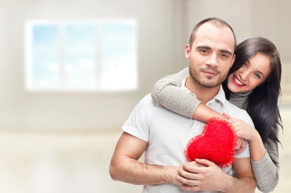 Retrato de pareja joven con el corazón rojo de pie en su casa y abrazando — Foto de Stock