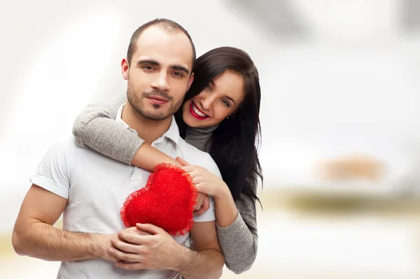 Πορτρέτο του νεαρό ζευγάρι με κόκκινη καρδιά στέκεται στο σπίτι τους και αγκαλιάζουν — Φωτογραφία Αρχείου