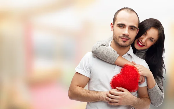 Portrait of young couple with red heart standing at their home and embracing. They are really happy to be together — Stock Photo, Image
