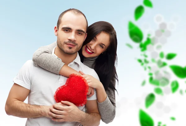 Счастливая взрослая пара с красным сердцем на заднем плане с зелеными листьями, обнимающая и смеющаяся — стоковое фото