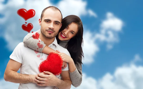 Szczęśliwa młoda para dorosłych z czerwonym sercem na romantyczny tło niebo i chmury, obejmując i śmiejąc się — Zdjęcie stockowe