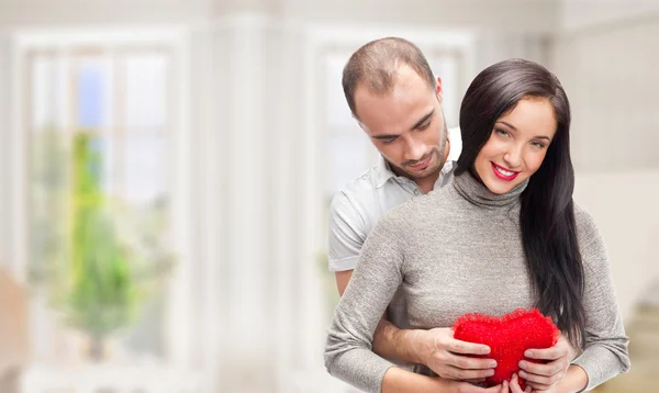 Portrait of young couple with red heart standing at their home and embracing — Stock Photo, Image