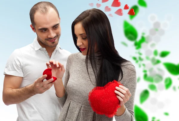 Propuesta de matrimonio: hombre joven poniendo anillo en el dedo joven ladys, sobre fondo romántico con corazones rojos y hojas verdes — Foto de Stock