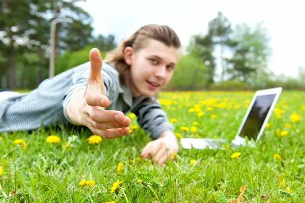 一个快乐的年轻人躺在花园和使用的便携式计算机-室外的肖像 — 图库照片