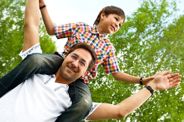 Portret ojca uśmiechający się podając jego syn piggyback jeździć na zewnątrz niebo i drzewa w parku — Zdjęcie stockowe