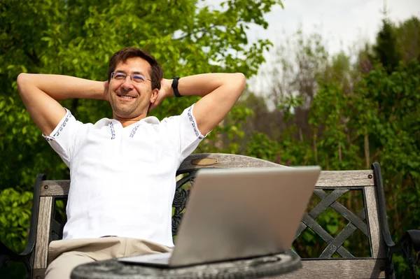 Porträtt av en ung man med laptop utomhus sitter på bänken — Stockfoto